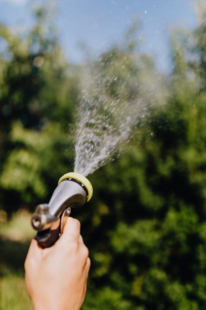 Close-up of hand holding a hose, spraying water with green background. Perfect for garden and outdoor concepts.